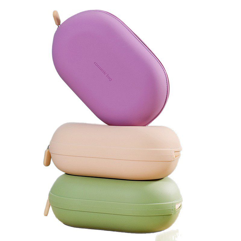 Minimalist pebble-shaped silicone makeup pouches in sage green, lavender, and cream, displayed on aesthetic white blocks for modern travel organization.