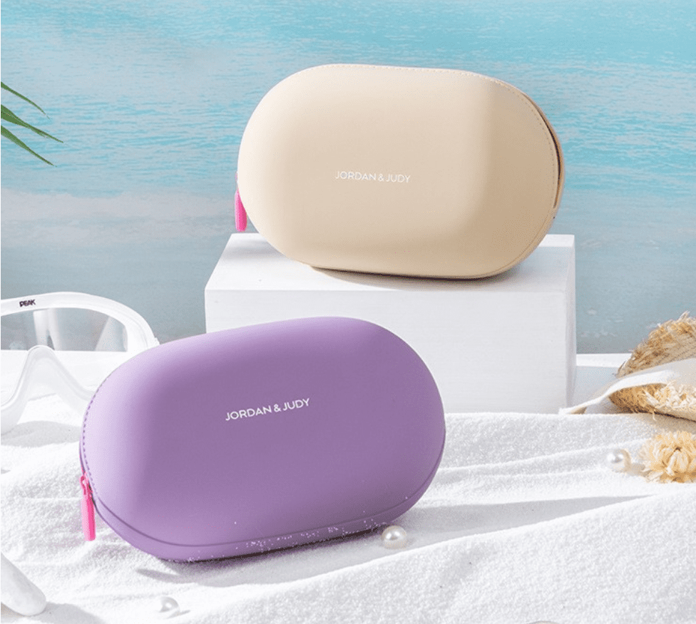 Minimalist pebble-shaped silicone makeup pouches in sage green, lavender, and cream, displayed on aesthetic white blocks for modern travel organization.