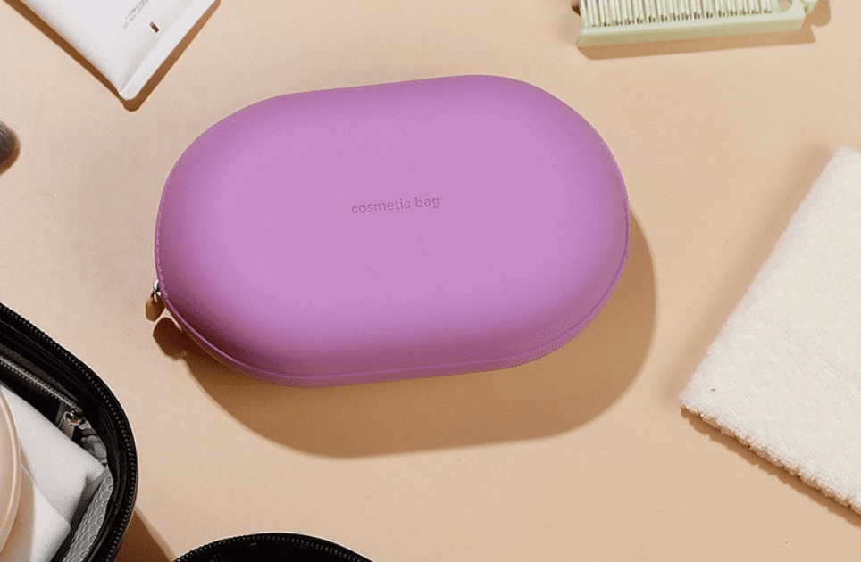 Minimalist pebble-shaped silicone makeup pouches in sage green, lavender, and cream, displayed on aesthetic white blocks for modern travel organization.