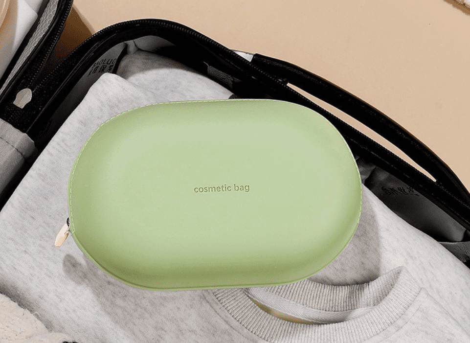 Minimalist pebble-shaped silicone makeup pouches in sage green, lavender, and cream, displayed on aesthetic white blocks for modern travel organization.